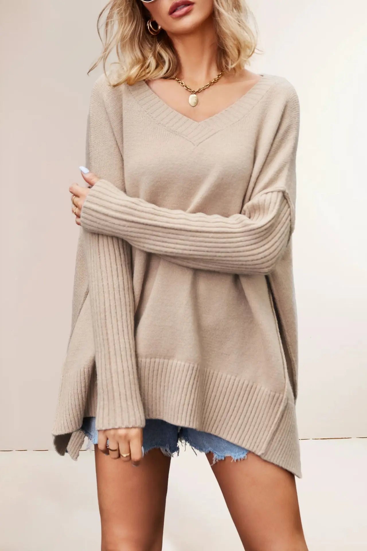 Woman wearing a beige sweater and denim shorts against a plain background