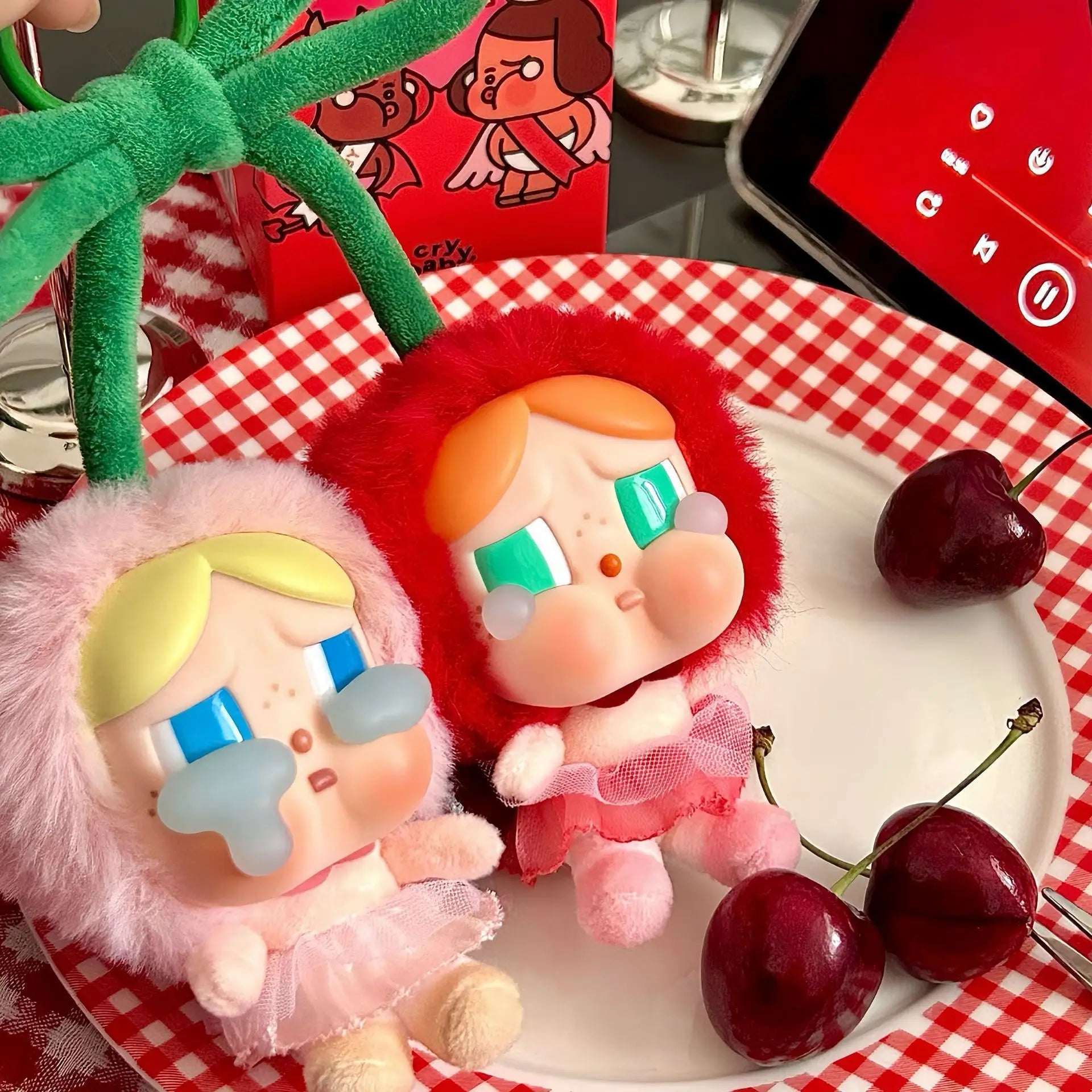 Pop Mart Cry baby, love you cherry much. Two cartoon-style dolls on a plate with cherries and a smartphone displaying a keyboard.