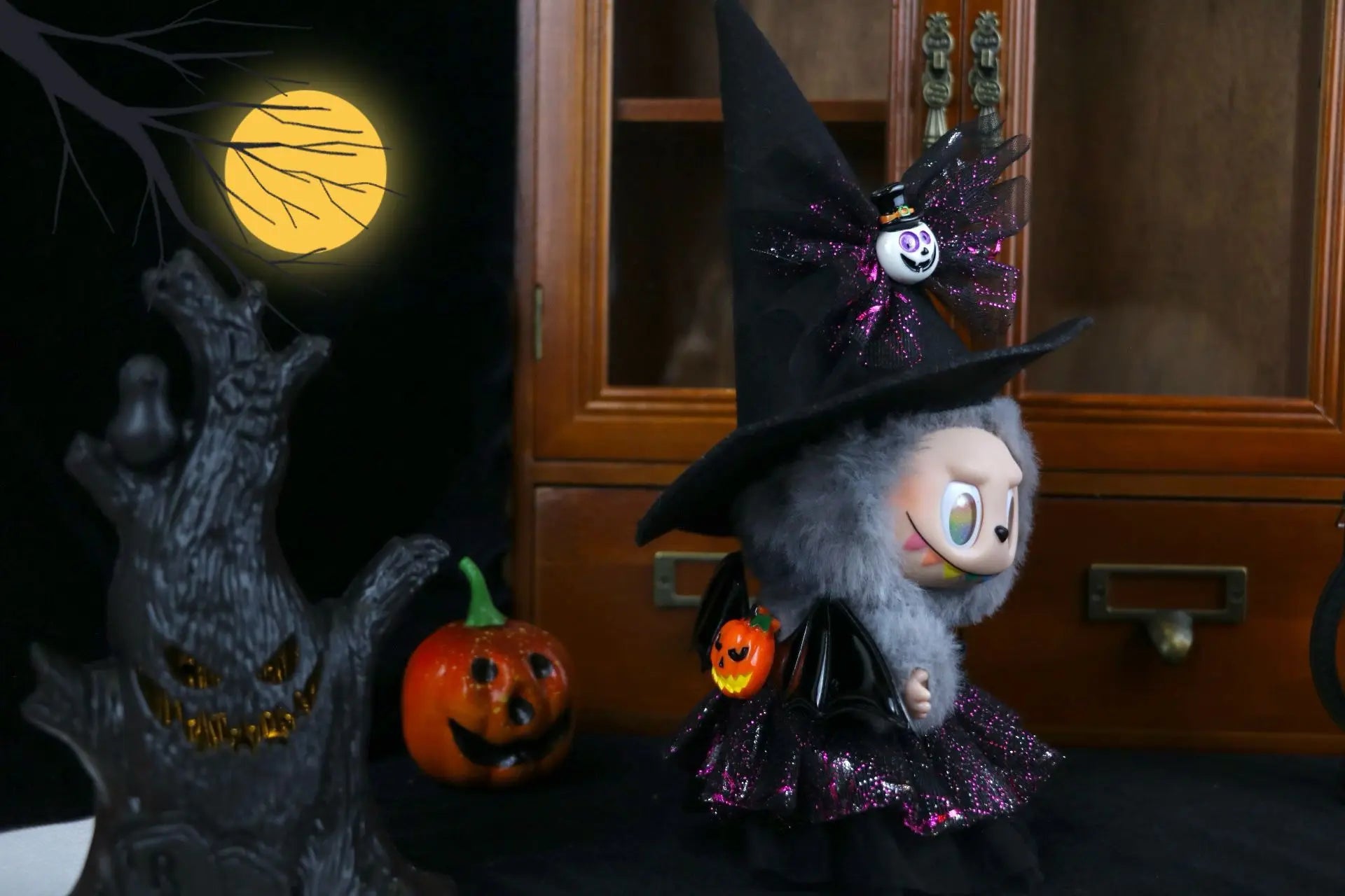 Labubu Halloween dress. Halloween-themed decoration with a plush toy in a witch hat, jack-o'-lantern, and ghost.