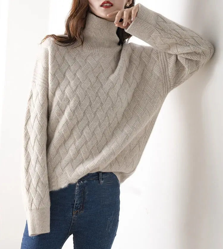 Person wearing a beige cable knit sweater and blue jeans against a white background