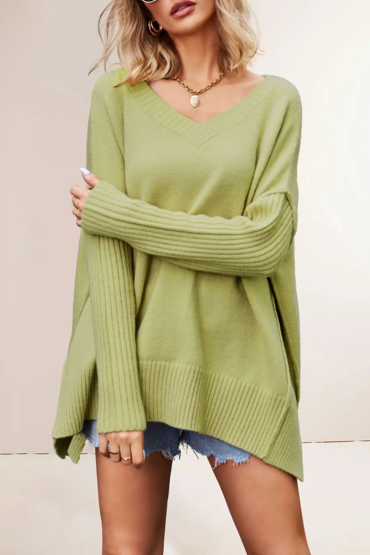 Woman wearing a green sweater and denim shorts against a plain background