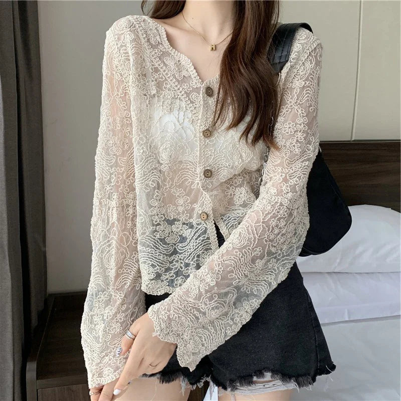 Person wearing a beige lace cardigan over a black outfit in an indoor setting.