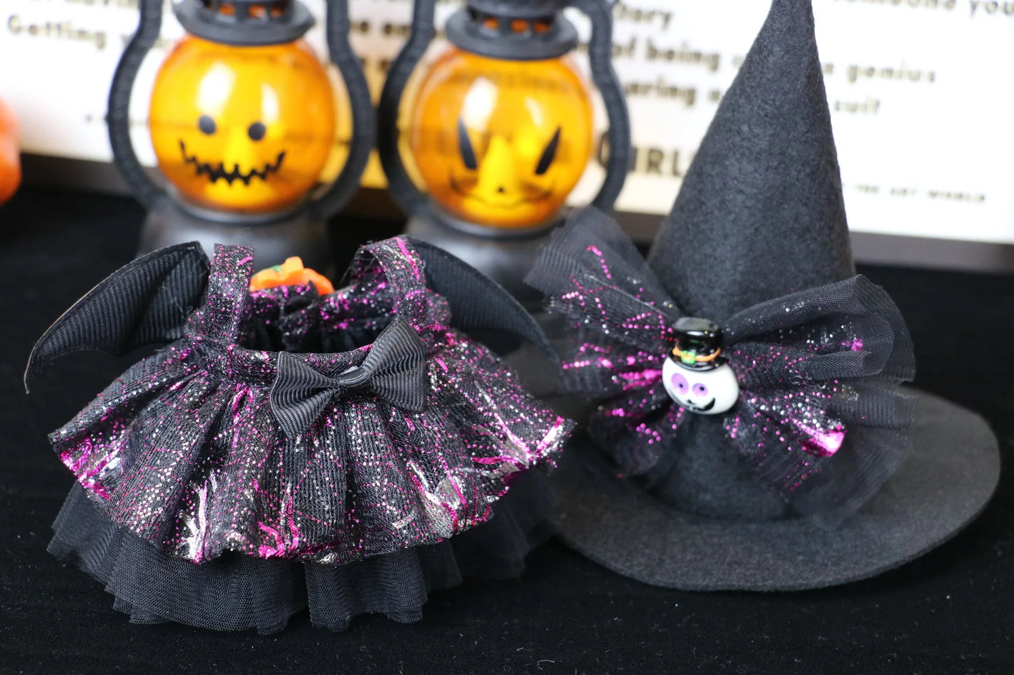 Labubu Halloween dress. Halloween-themed pet accessories including a black witch hat and dress with glittery details on a dark surface.