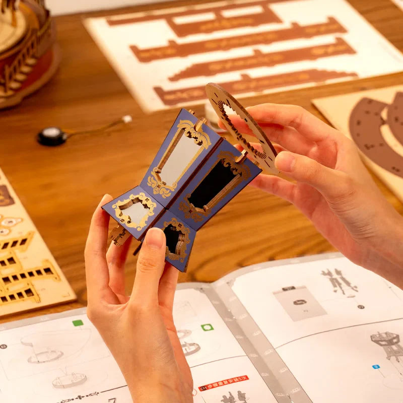 Hands holding a small wooden model kit with intricate details on a wooden table.