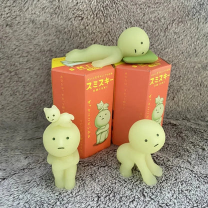 Smiski, living room series. Three green plush toys on top of red boxes with Japanese text against a gray textured background