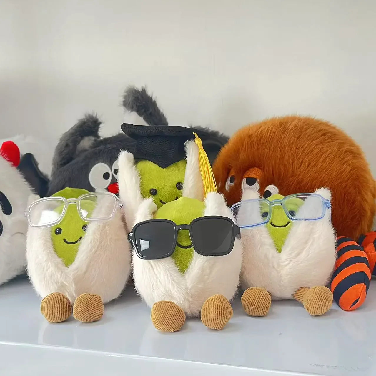  pistachio. Plush toys resembling llamas with glasses and a spider on a white surface