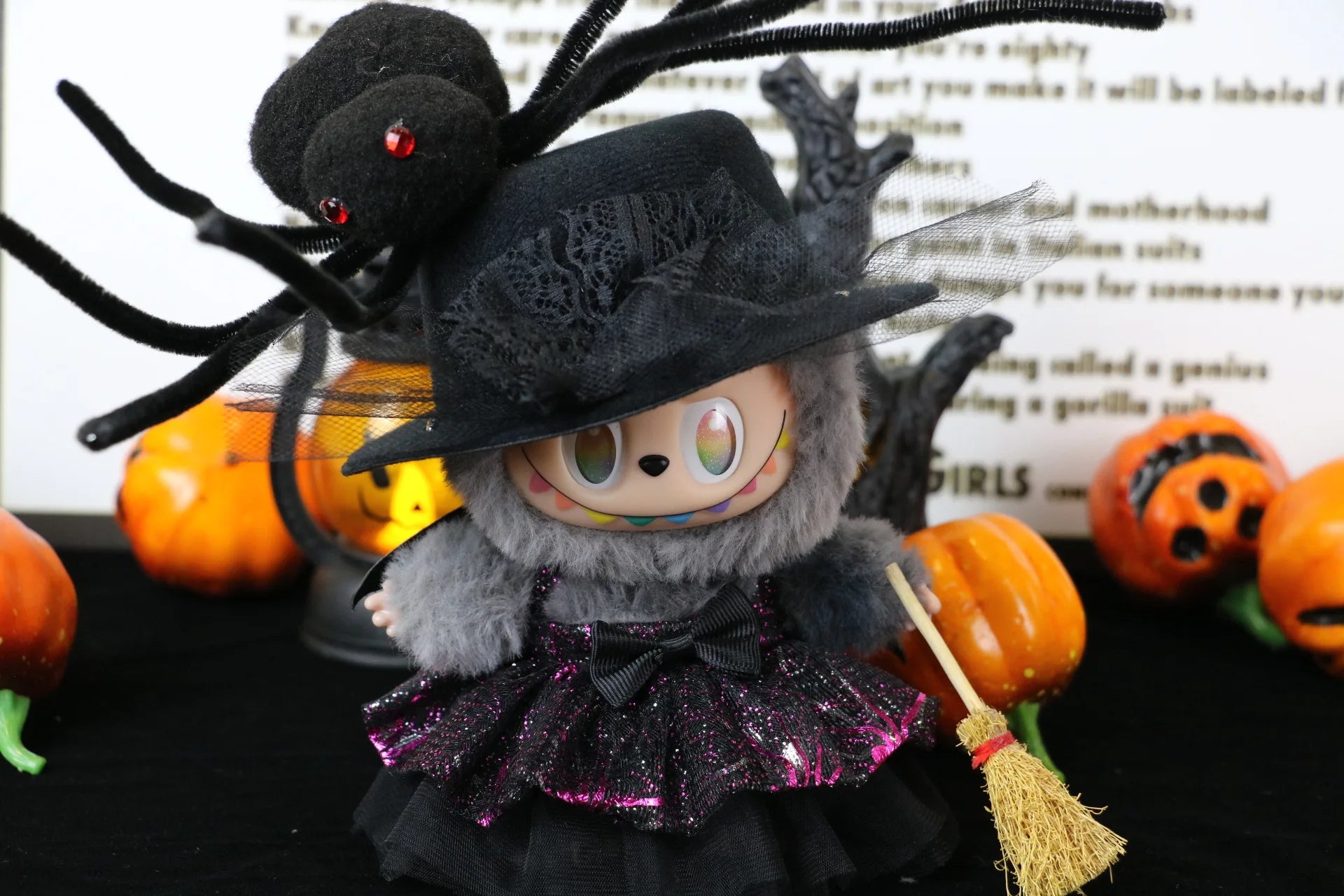 Labubu Halloween dress. Halloween-themed plush toy with spider and broom, surrounded by pumpkins and text.