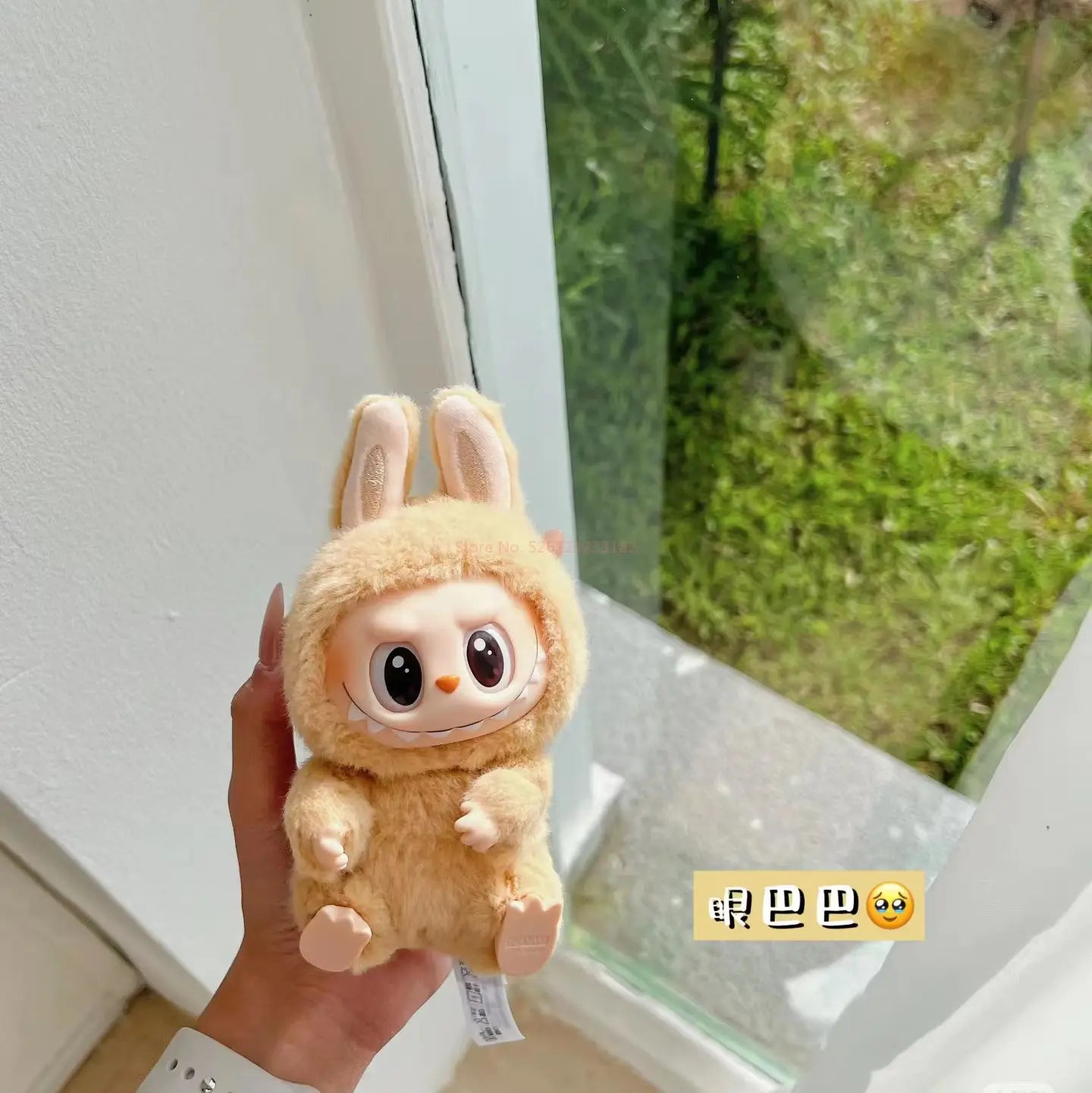 Plush toy labubu held by a hand with a window in the background