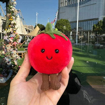 Jellycate. Plush tomato toy held in front of a cityscape with flowers and a building.
