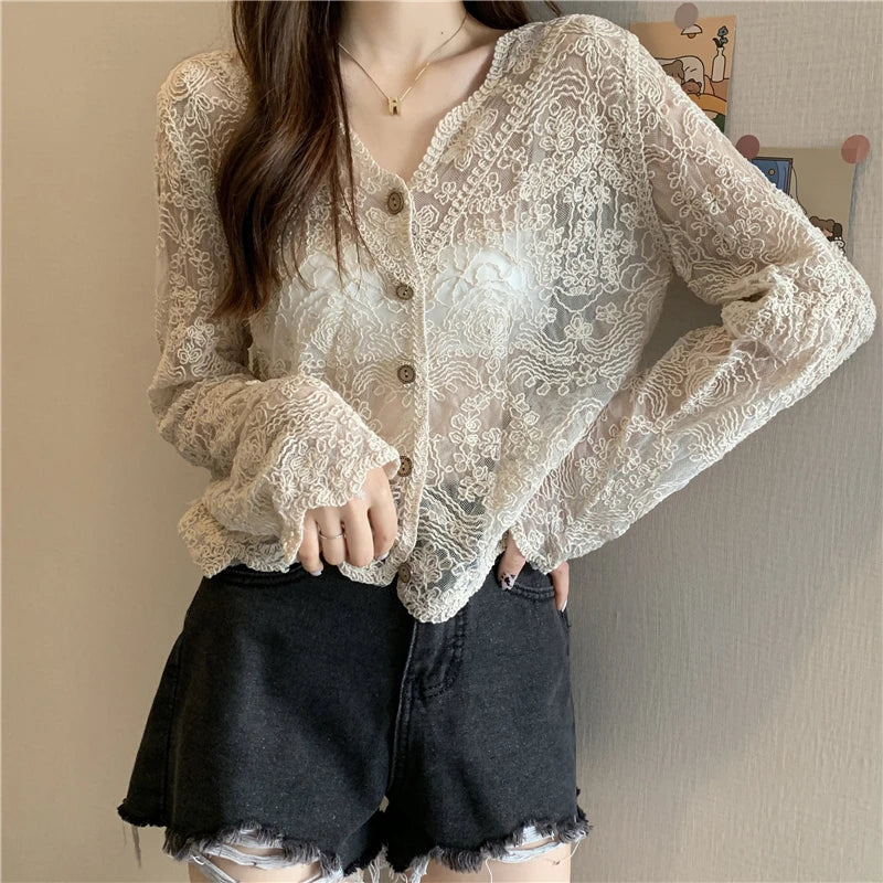 Person wearing a beige lace blouse and black shorts against a neutral background