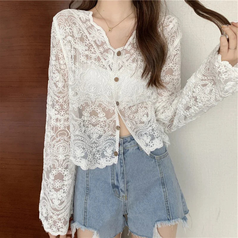 Person wearing a white lace blouse with sheer sleeves and denim shorts against a neutral background