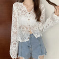 Person wearing a white lace blouse with sheer sleeves and denim shorts against a neutral background