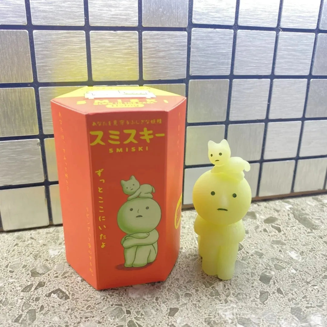 Yellow plush toy with a box labeled 'SMISKI' on a tiled floor.