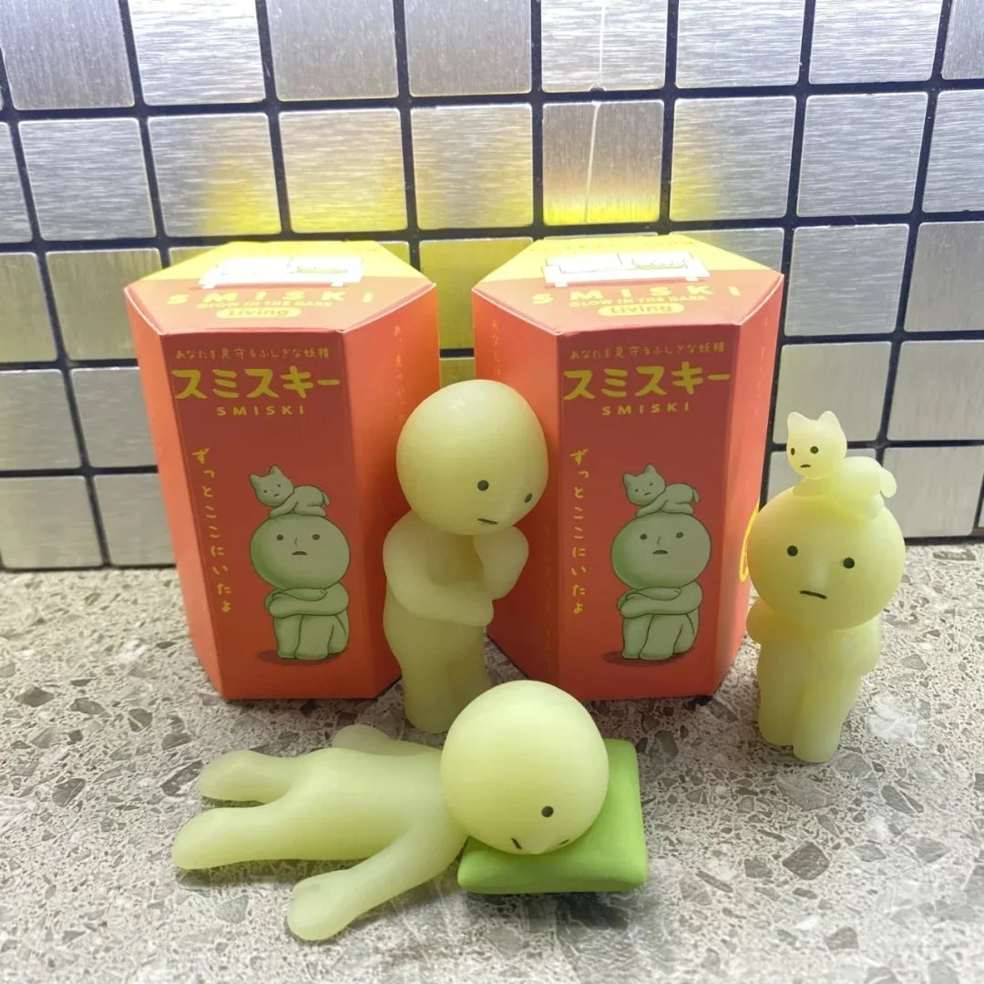Smiski, living room series. Two green plush toys in front of red boxes with cartoon characters on a tiled floor.