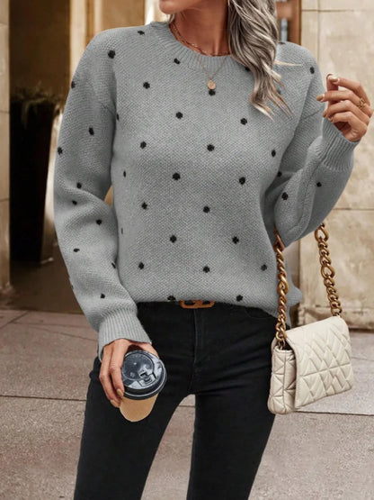 Woman wearing a gray sweater with black polka dots, holding a coffee cup and a beige handbag.