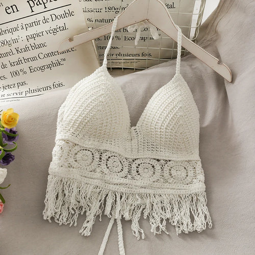 White crochet bralette with fringe on a hanger against a neutral background