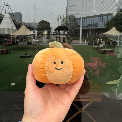 Jellycat. Hand holding a small plush pumpkin toy with a blurred outdoor background 