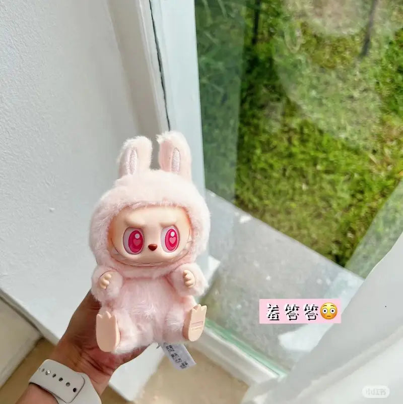 Labubu have a seat. Pink plush toy with large red eyes held by a hand near a window.