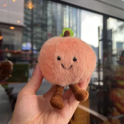 Jellycate.Plush toy resembling a peach held in a hand with a blurred cityscape background