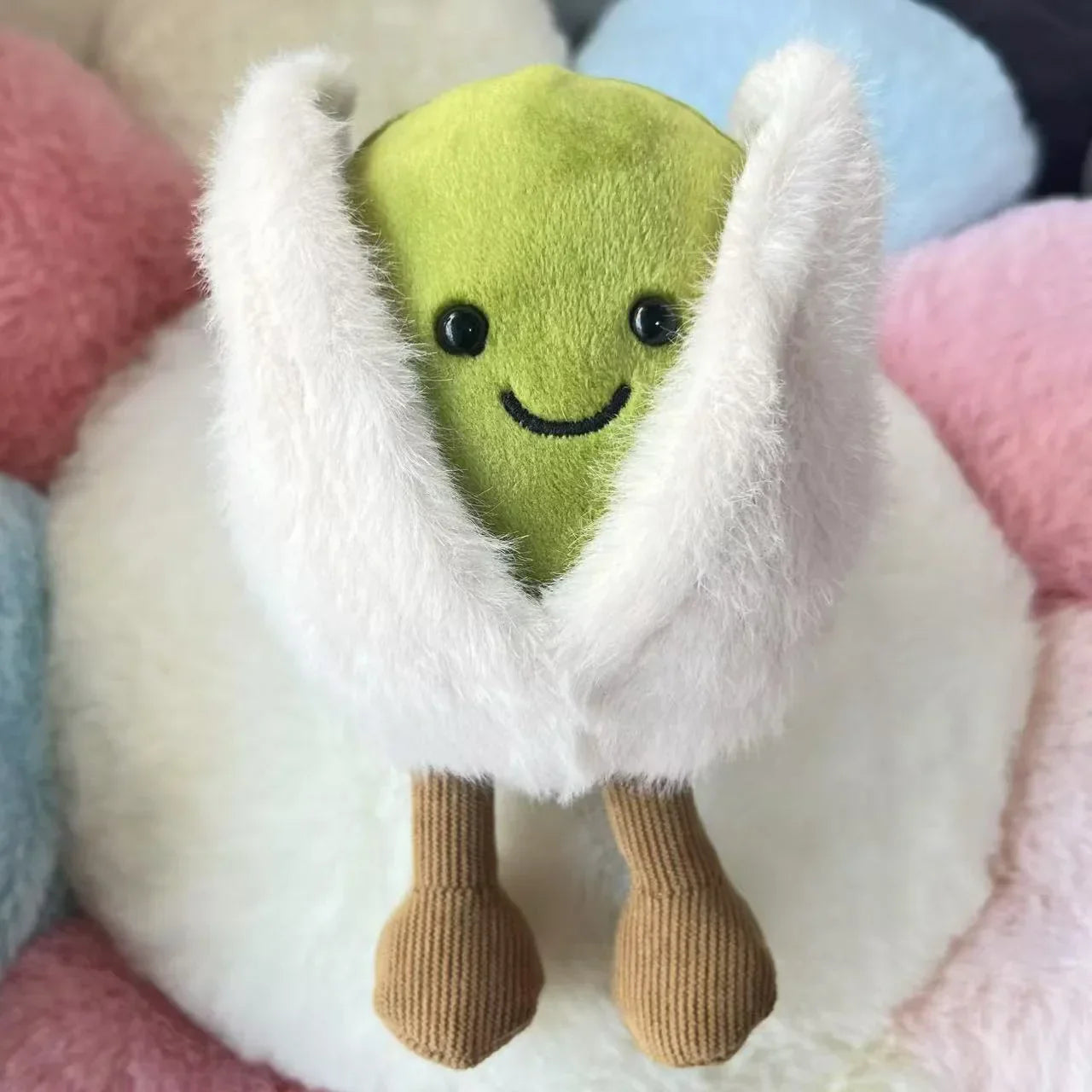  pistachio. Green plush toy with a white hood on a soft, multicolored background