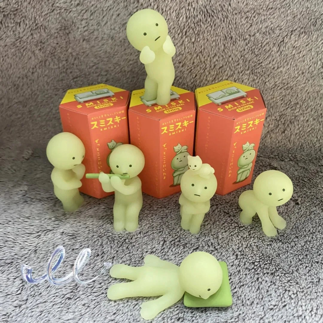 Smiski, living room series. Set of green plush toys resembling small creatures on red boxes with Japanese text, on a textured gray surface.
