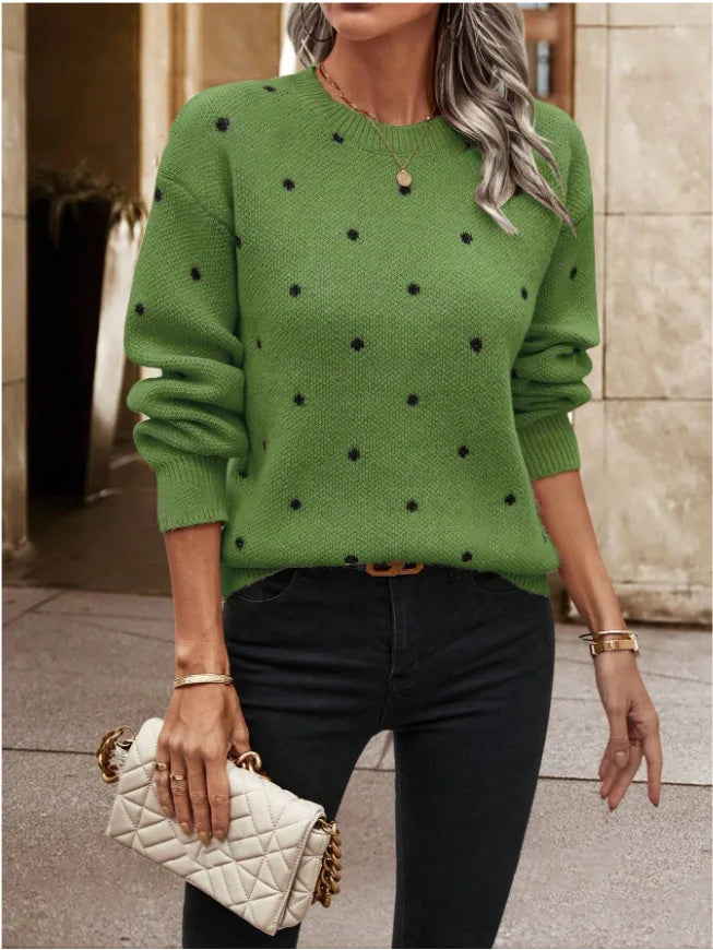 Person wearing a green sweater with black polka dots, holding a white quilted handbag.