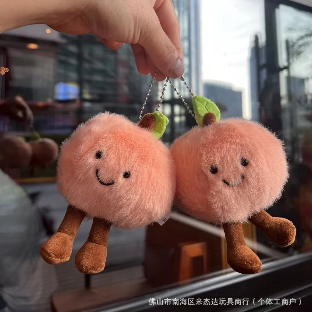 Two plush peach-shaped keychains held by a hand with a blurred background.