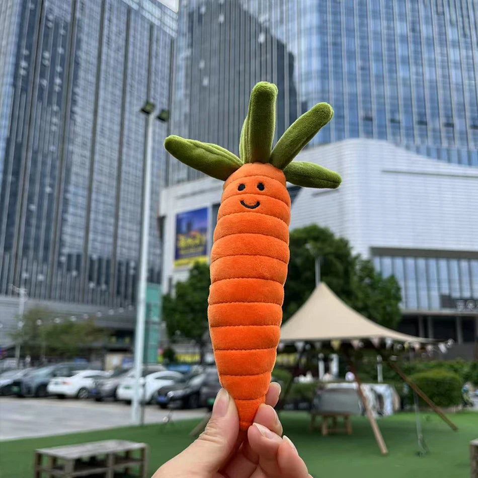 Jellycat. Carrot-shaped toy held in front of a cityscape with tall buildings.