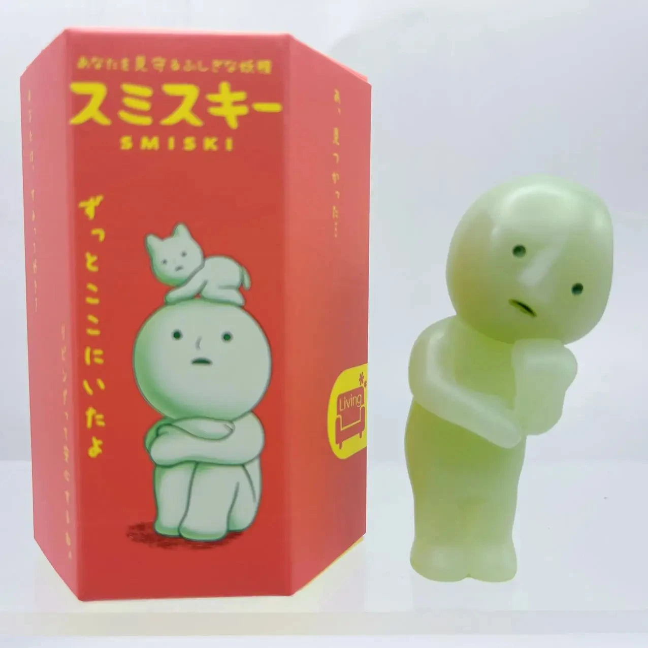Smiski, living room series. Green figurine next to its red packaging with cartoon character illustration