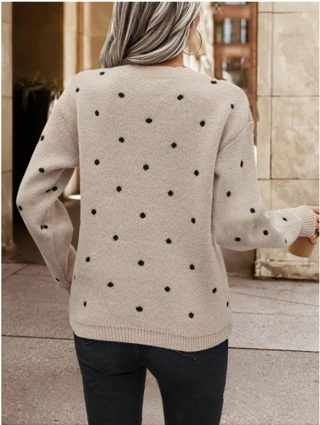 Person wearing a beige sweater with black polka dots, standing in an outdoor setting.