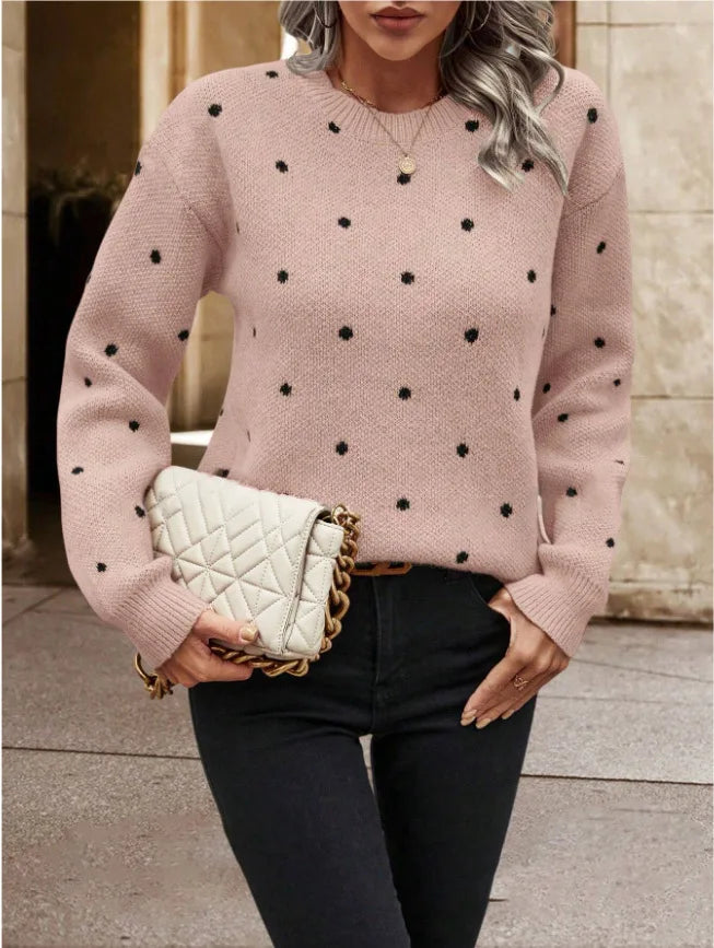 Person wearing a pink sweater with black polka dots, holding a white quilted handbag.