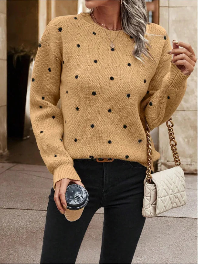 Person wearing a mustard yellow sweater with black polka dots, holding a beige handbag and a drink.