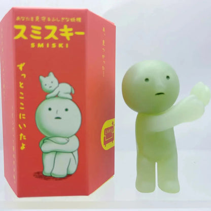 Smiski, living room series. Green figurine next to its red box with cartoon design and text