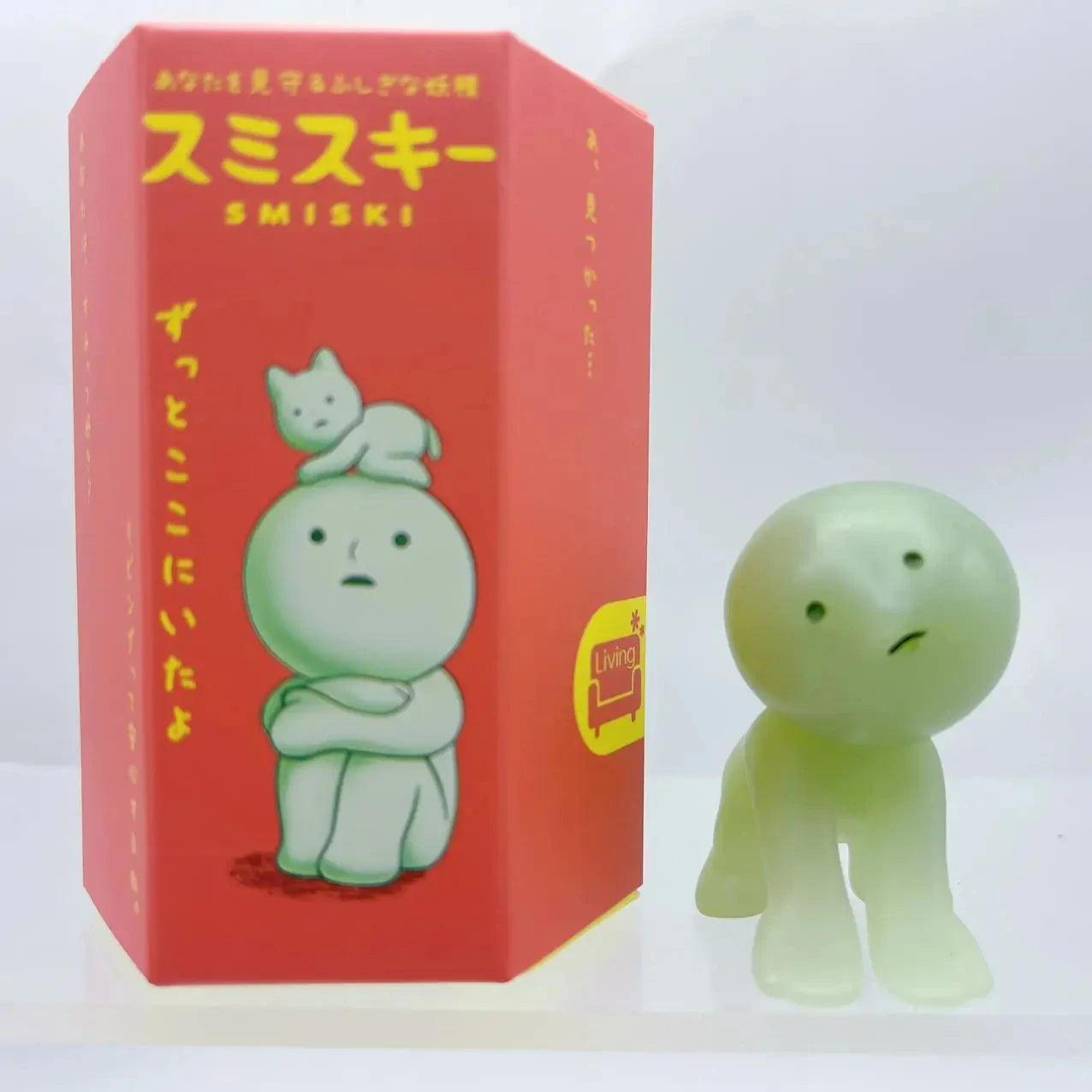 Smiski, living room series. Green figurine next to its red box with cartoon character design on a white background