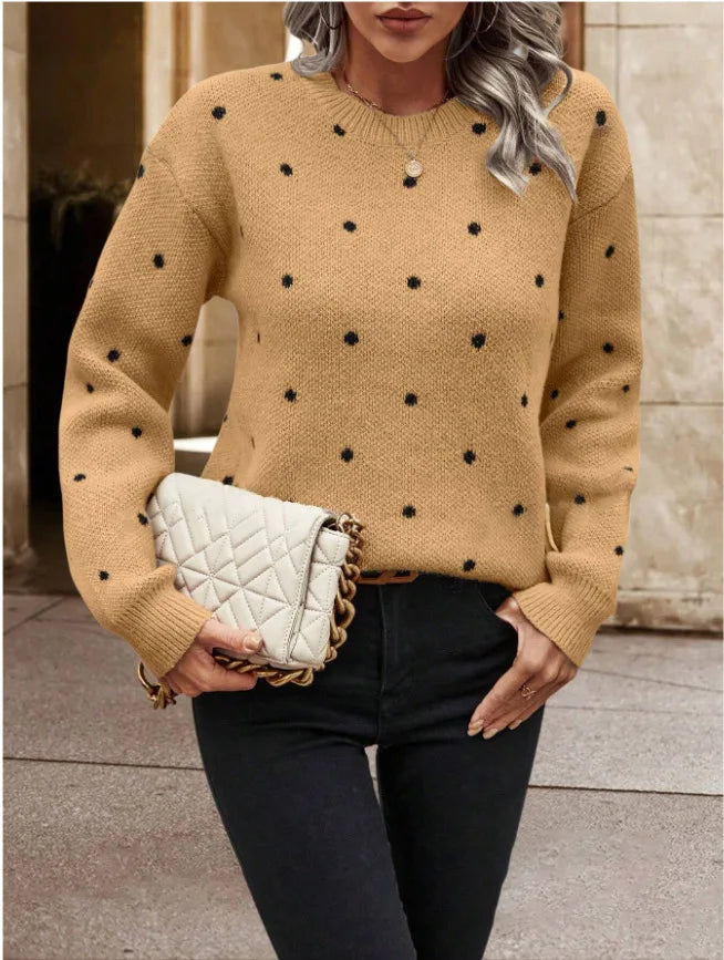 Woman wearing a beige sweater with black polka dots, holding a white quilted handbag.