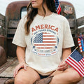 Person wearing a 'America 250 Years Strong' t-shirt with an American flag design, sitting in front of a vintage truck.