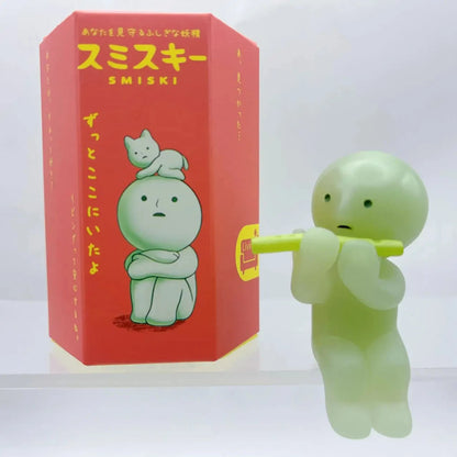 Smiski, living room series. Green Smiski figurine with red packaging featuring cartoon character and text.