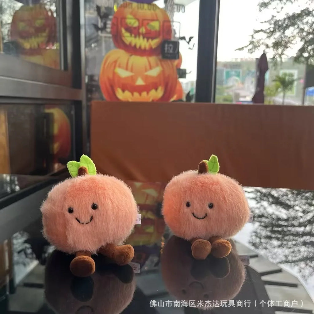  Two plush pumpkins with smiling faces on a reflective surface, with Halloween decorations in the background.