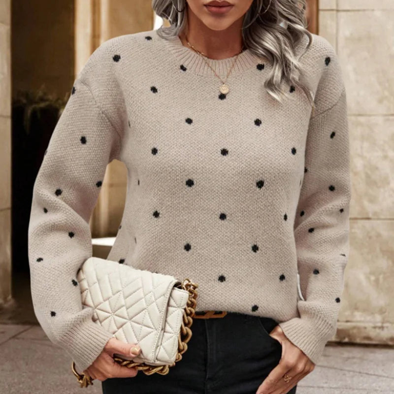 Woman wearing a beige sweater with black polka dots, holding a cream handbag.