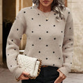 Woman wearing a beige sweater with black polka dots, holding a cream handbag.