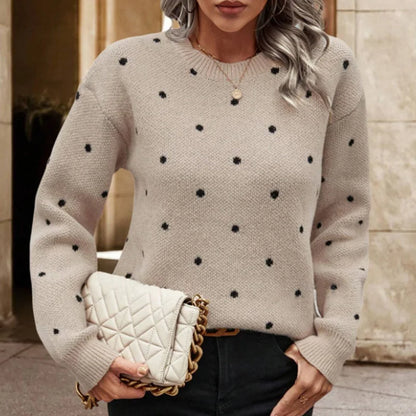 Woman wearing a beige sweater with black polka dots, holding a cream handbag.