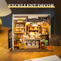 Miniature bakery model with 'Bakery & Desserts' sign, illuminated inside, on a wooden surface.