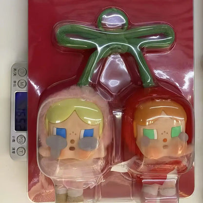 Pop Mart Cry baby, love you cherry much. Two cartoon character figurines in clear packaging on a digital scale with a red background.
