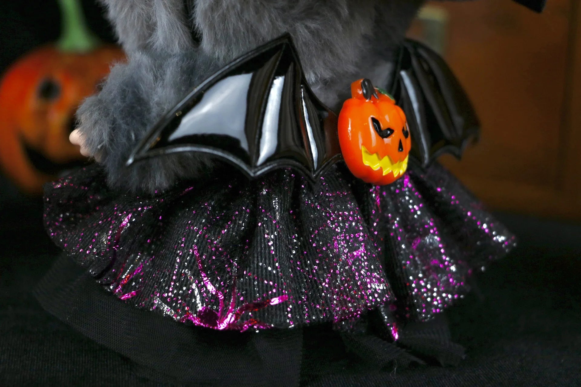Labubu Halloween dress. Labubu wearing a Halloween costume with bat wings and pumpkin, with pumpkins in the background.