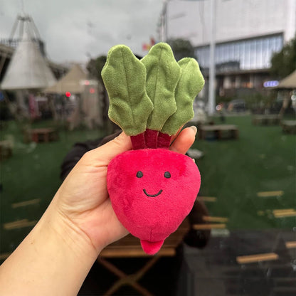 Jellycat. Hand holding a pink radish-shaped plush toy with green leaves against an outdoor background.