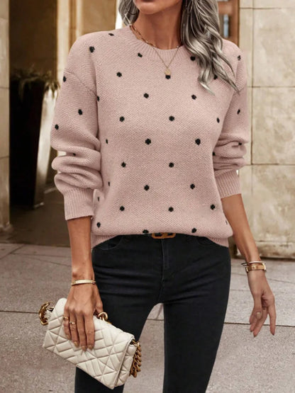 Woman wearing a pink sweater with black polka dots, holding a white quilted handbag.