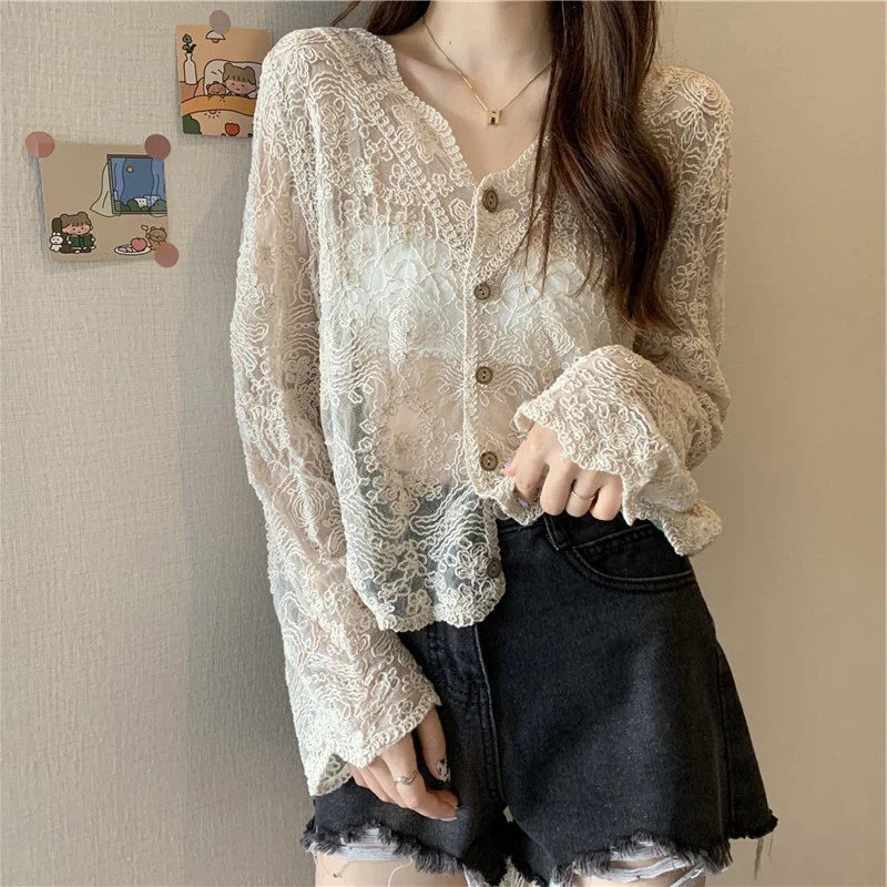 Person wearing a lace blouse and black shorts against a neutral wall.